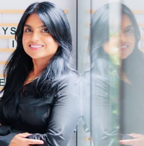 Mona Kumar leaning on glass panel. 